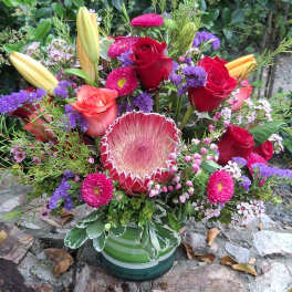 Mixed bouquet with red roses, lilies, and a protea in a striped vase