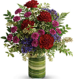 Red and purple flowers arranged in a green glass vase
