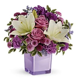 Purple and white floral arrangement in a lavender glass vase
