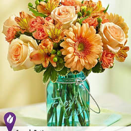 Peach roses and orange daisies in a turquoise glass jar