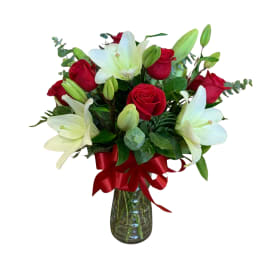 Red roses and white lilies in a glass vase with a red ribbon