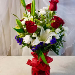 Red roses and white lilies in a red glass vase with a ribbon