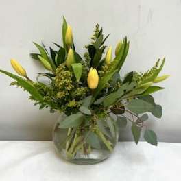 Yellow tulip arrangement with foliage in a round clear glass vase