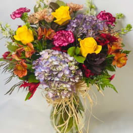 Mixed bouquet of roses, hydrangeas, and carnations in a glass vase
