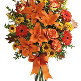 Orange lilies and mixed fall flowers in a glass vase with an orange ribbon