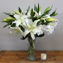 White lilies in a clear glass vase with a small candle beside it