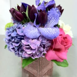 Bouquet of purple hydrangeas, dark tulips, pink roses, and calla lilies in a square vase