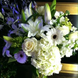 Tall white floral arrangement with lilies, roses, hydrangeas, and gerbera daisies in a clear glass vase
