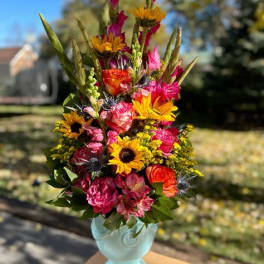 Tall mixed bouquet in a light blue vase with bright pink and yellow flowers