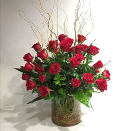 Red roses arranged in a clear glass vase with tall curly branches