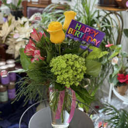 Birthday bouquet with yellow roses, pink flowers, and a purple sign in a glass vase