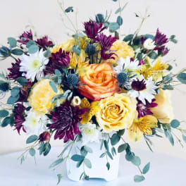 Bouquet of yellow and purple flowers in a white container