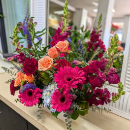 Bright arrangement of hot pink gerbera daisies, peach roses, and burgundy snapdragons with blue hydrangea accents