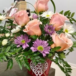 Pink roses and purple daisies in a red heart-decorated basket