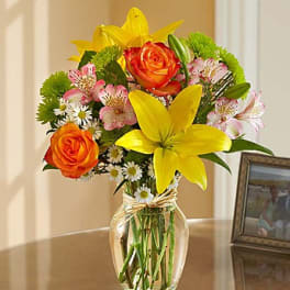 Bouquet of yellow lilies, orange roses, and pink alstroemeria in a glass vase