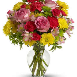Mixed bouquet of pink roses, red carnations, and yellow daisies in a clear glass vase