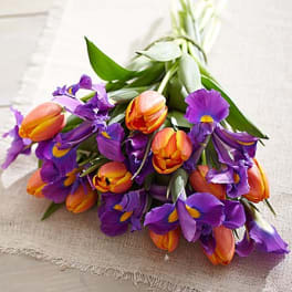 Bouquet of orange tulips and purple irises on a light fabric surface