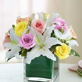Bouquet of pastel roses and white lilies in a clear square vase