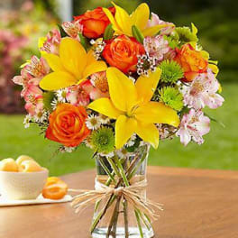 Bouquet of yellow lilies, orange roses, and pink alstroemeria in a glass vase