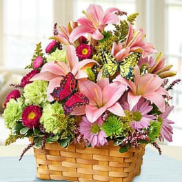 Pink lilies and mixed daisies in a woven basket with butterfly picks