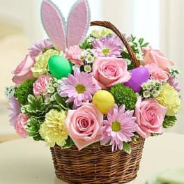 Basket of pink roses and daisies with pastel Easter eggs and bunny ears