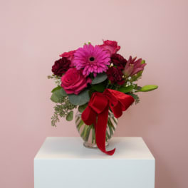 Pink and red flower bouquet in a glass vase with a red ribbon