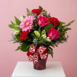 Pink and red mixed bouquet in a glass vase with a heart ribbon