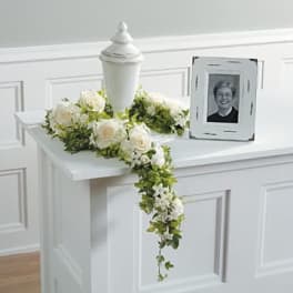 White rose floral tribute draped over a white urn