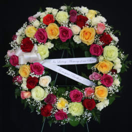 Heart-shaped wreath of multicolored roses with a memorial ribbon