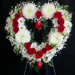 Heart-shaped floral wreath with red roses and white flowers on a stand