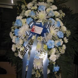 Standing sympathy wreath with white mums and blue roses on an easel with blue ribbons