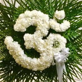 White floral heart wreath with a ribbon bow on a green palm backdrop