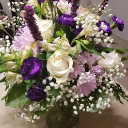 Bouquet of white roses, purple flowers, and pink daisies in a glass vase