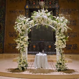 Tall white floral arch with matching column arrangements framing a small draped table