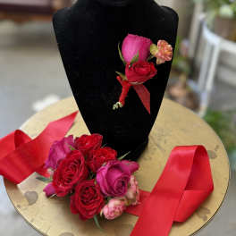 Red and pink rose boutonnieres with red ribbon on a black display stand