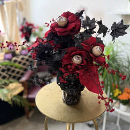 Dark red roses in a black vase with black foliage and eye-like accents