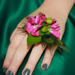 Pink floral wrist corsage with peacock feather accents on a hand