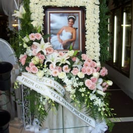 Funeral floral tribute with a framed portrait, white lilies, and pink roses