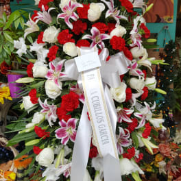 Large funeral wreath of red, white, and pink flowers with a white ribbon