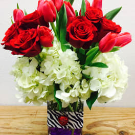 Red roses and pink tulips in a glass vase with white hydrangeas
