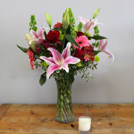 Pink lilies and red roses in a glass vase beside a small candle