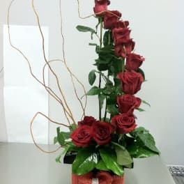 Tall arrangement of red roses in a black box with curly branches