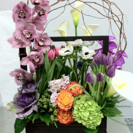 Mixed floral arrangement in a dark rectangular container with orchids and calla lilies