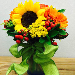 Sunflower and orange daisy bouquet in a glass vase with a green ribbon