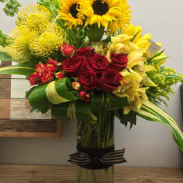 Bouquet of sunflowers, red roses, and yellow orchids in a tall glass vase