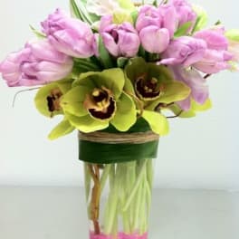 Pink tulips and green orchids arranged in a glass vase