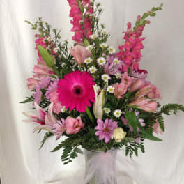 Pink mixed flower arrangement in a glass vase with a tulle bow
