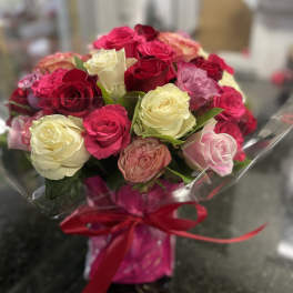 Bouquet of pink, red, and white roses wrapped in clear plastic with a red ribbon