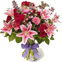 Pink lilies and red roses with small purple flowers in a clear vase with a purple bow