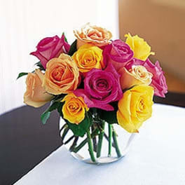 Compact arrangement of yellow, pink, and peach roses in a small clear glass bowl vase